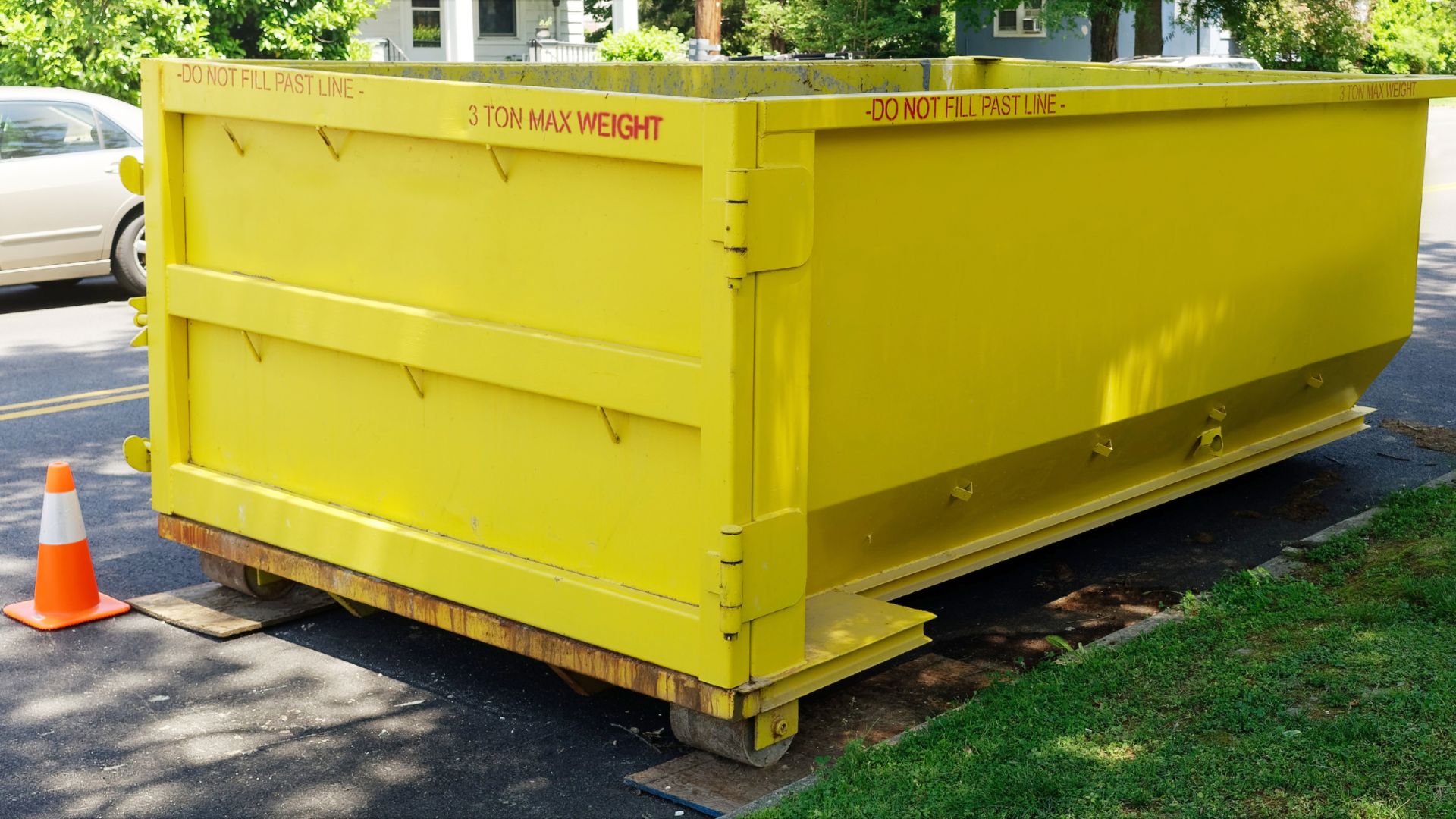 Large yellow dumpster with 3-ton weight limit parked on street near grass