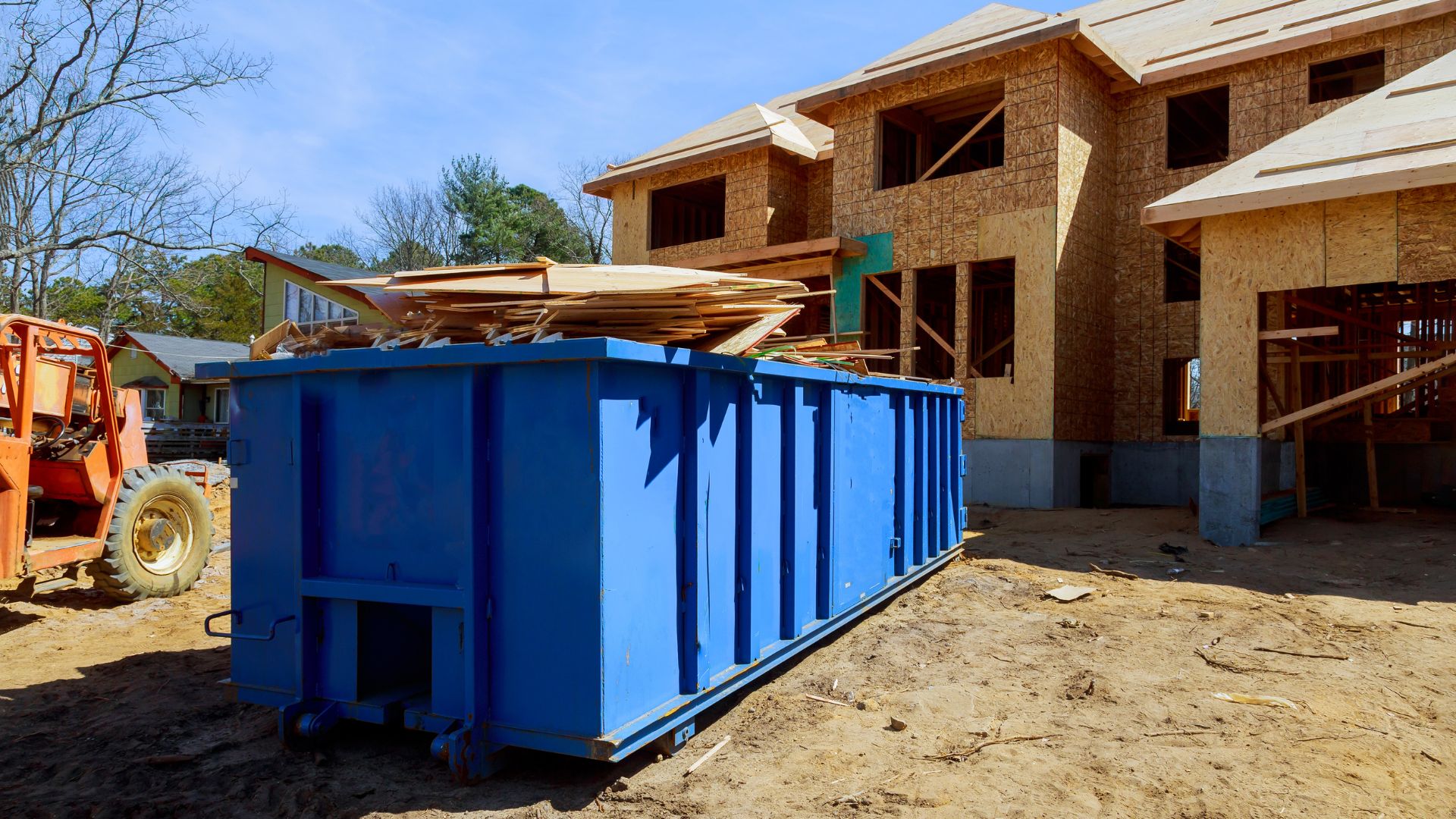 Blue dumpster at residential construction site with wooden framed houses